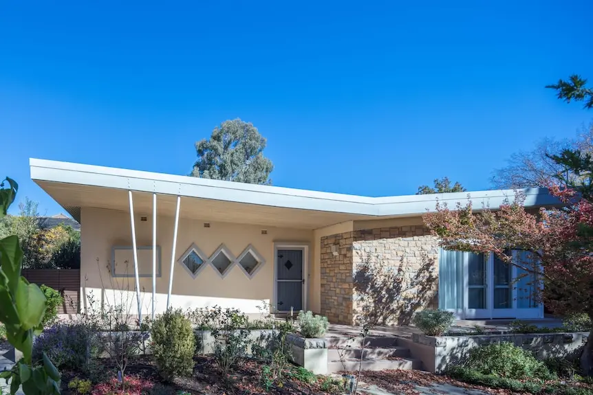 Photo of a home with stark geometric lines on roof, diamond shaped windows and dry shrubbery around it.