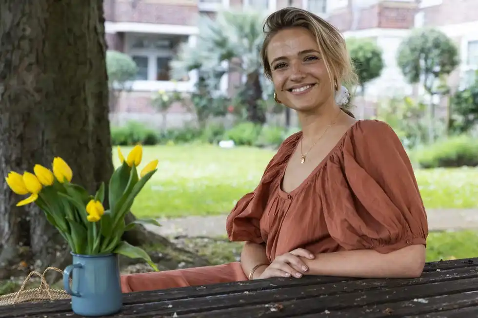 person seated at a table outdoors with a vase of yellow tulips