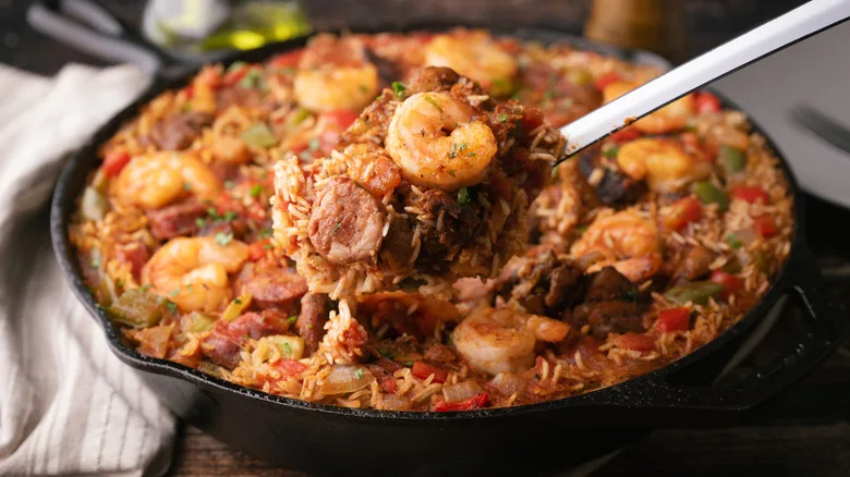 Spoon scooping jambalaya with shrimp and sasuage in cast iron pot