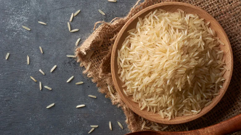 Bowl of uncooked basmati rice in wood bowl resting on piece of burlap on slate background