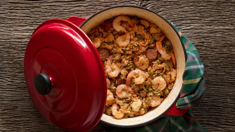 Top view of jambalaya in a red Dutch oven with and open lid on the side