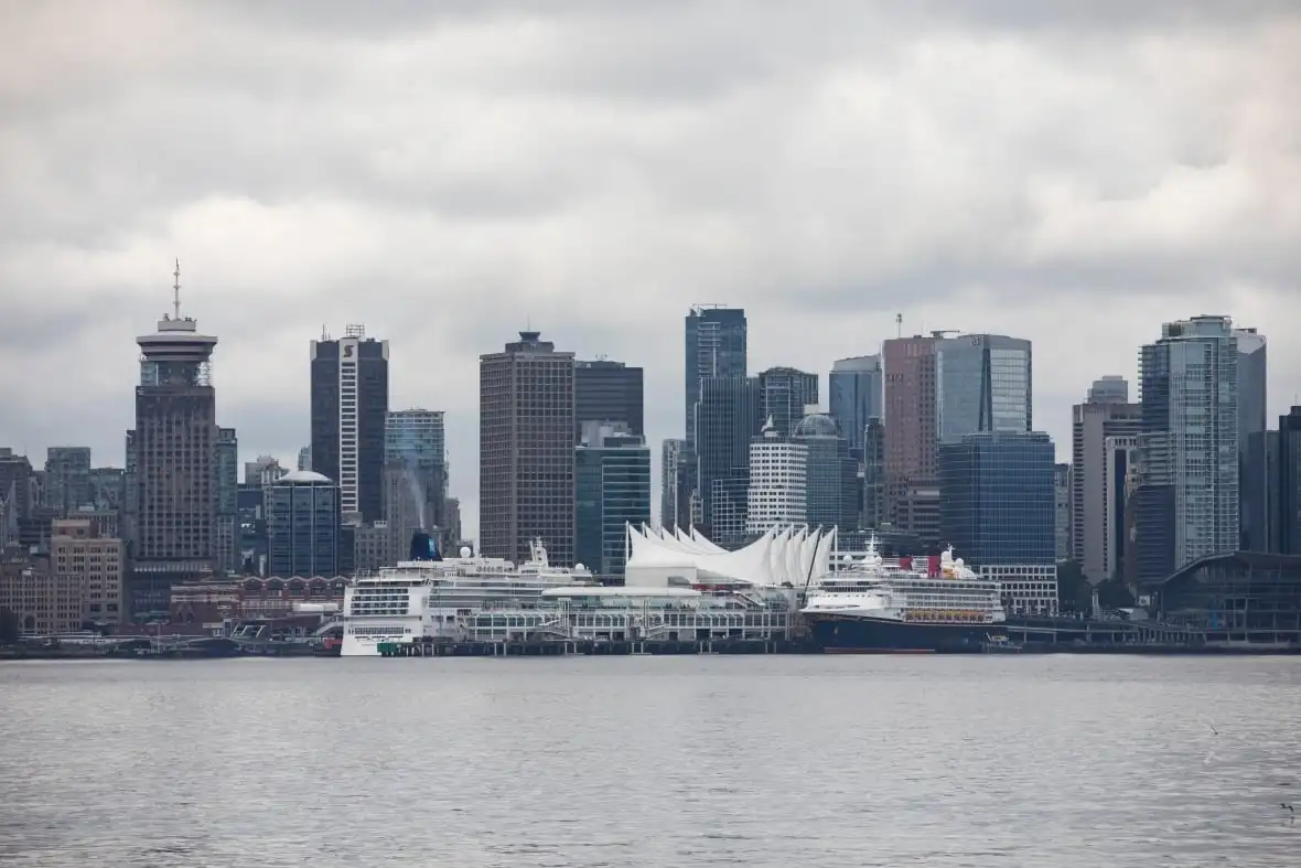 A downtown skyline with a series of skyscrapers, with two cruise ships and a convention centre with sails visible in the foreground.