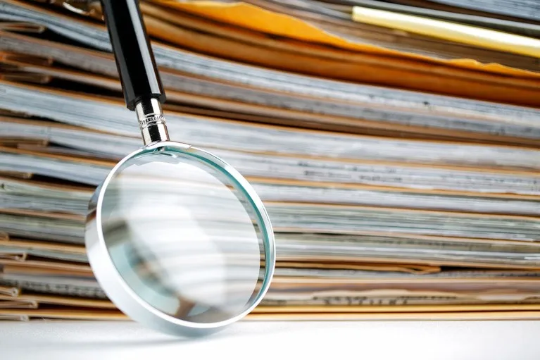 A magnifying glass resting against a tall stack of folders and paper documents.