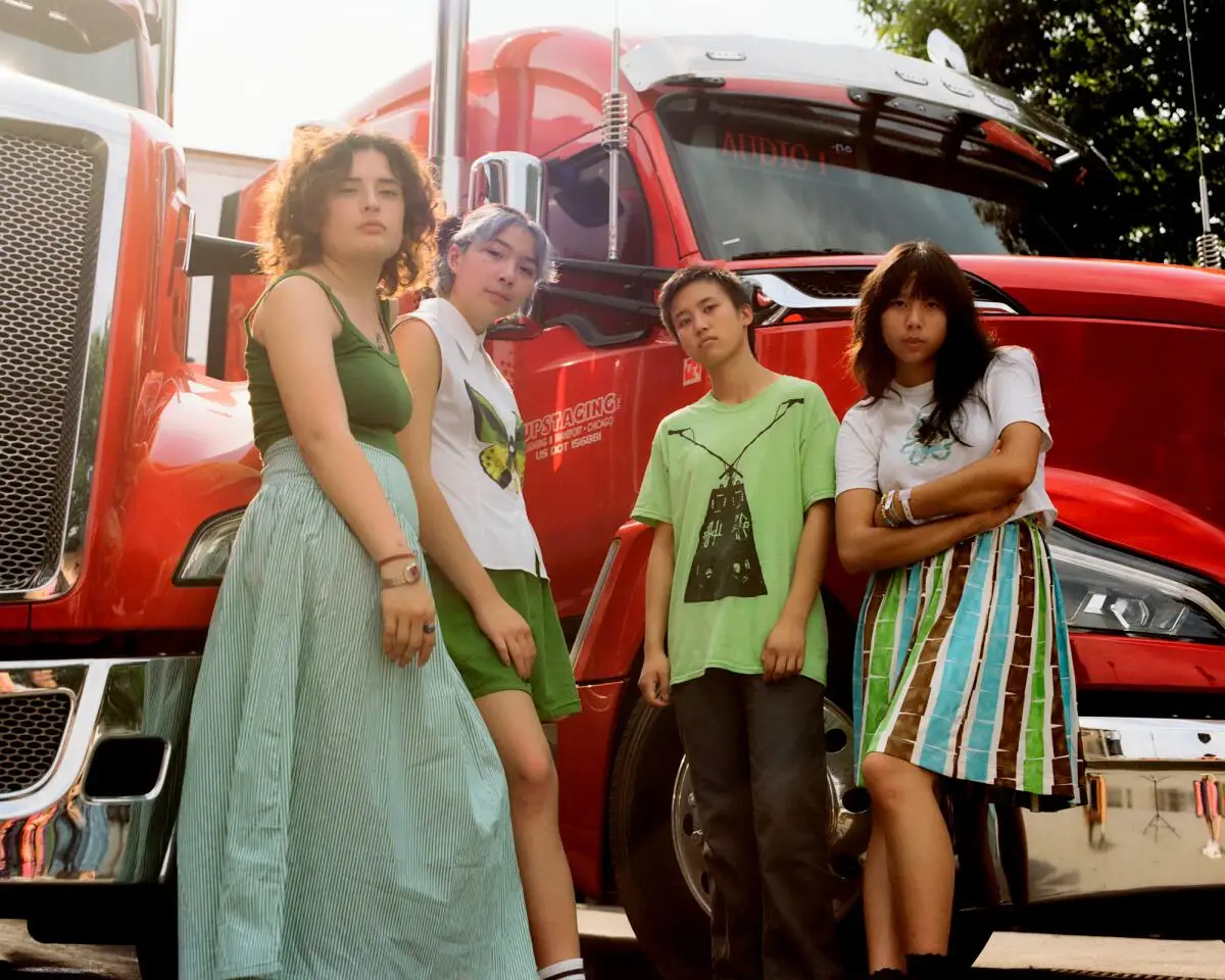 Four young women stand in front of a red semi truck.