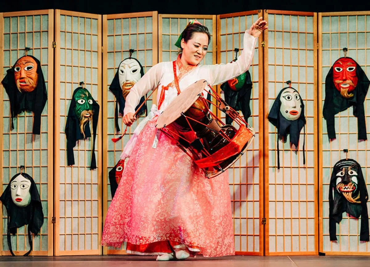 Alamed Post - a female performer holds a drum and performs onstage