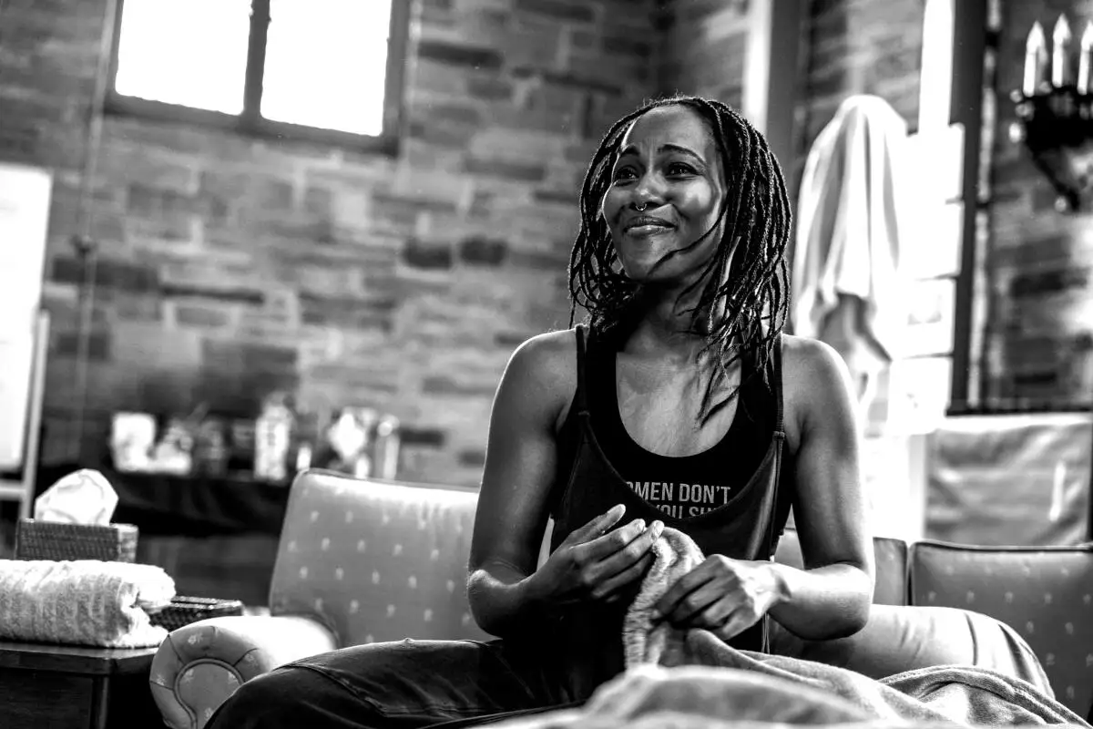 A woman in a black tank top smiles sitting on a couch onstage