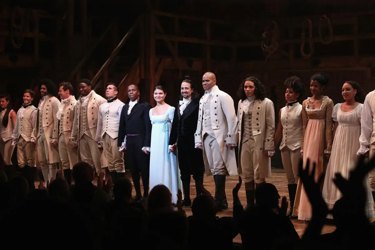 A line of actors in simplified 1700s costumes onstage for their bow