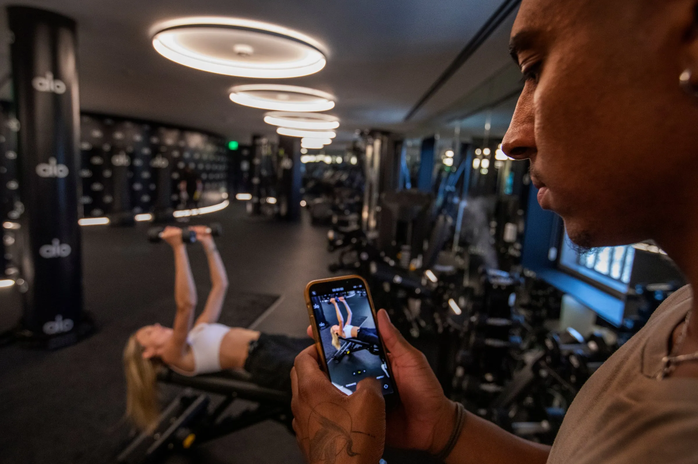 A man records a woman lifting weights.