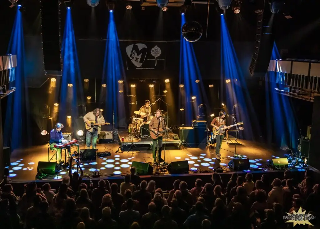 A 5-piece band, Gasoline Lollipops, play an indoor stage in front of a large crowd.