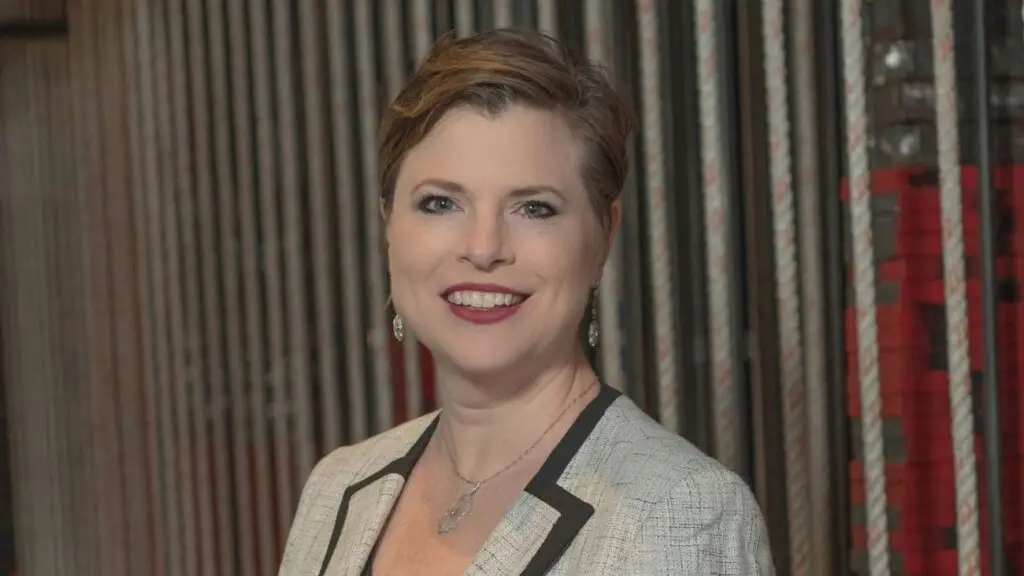 A headshot of Barbara Lynne Jamison, who has short brown hair and is wearing a black-trimmed tweed suit jacket.