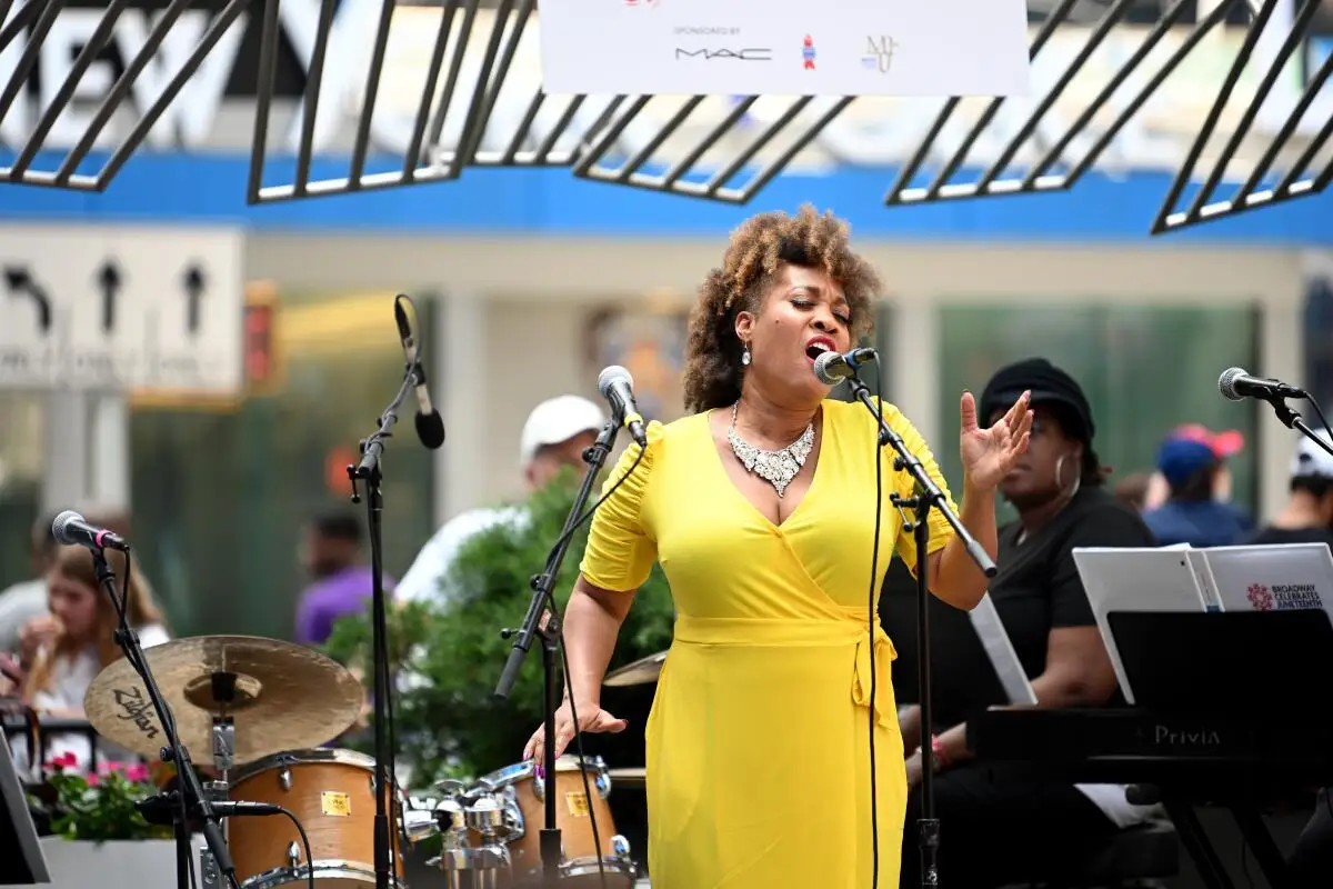 A woman in a yellow dress sings into a microphone onstage