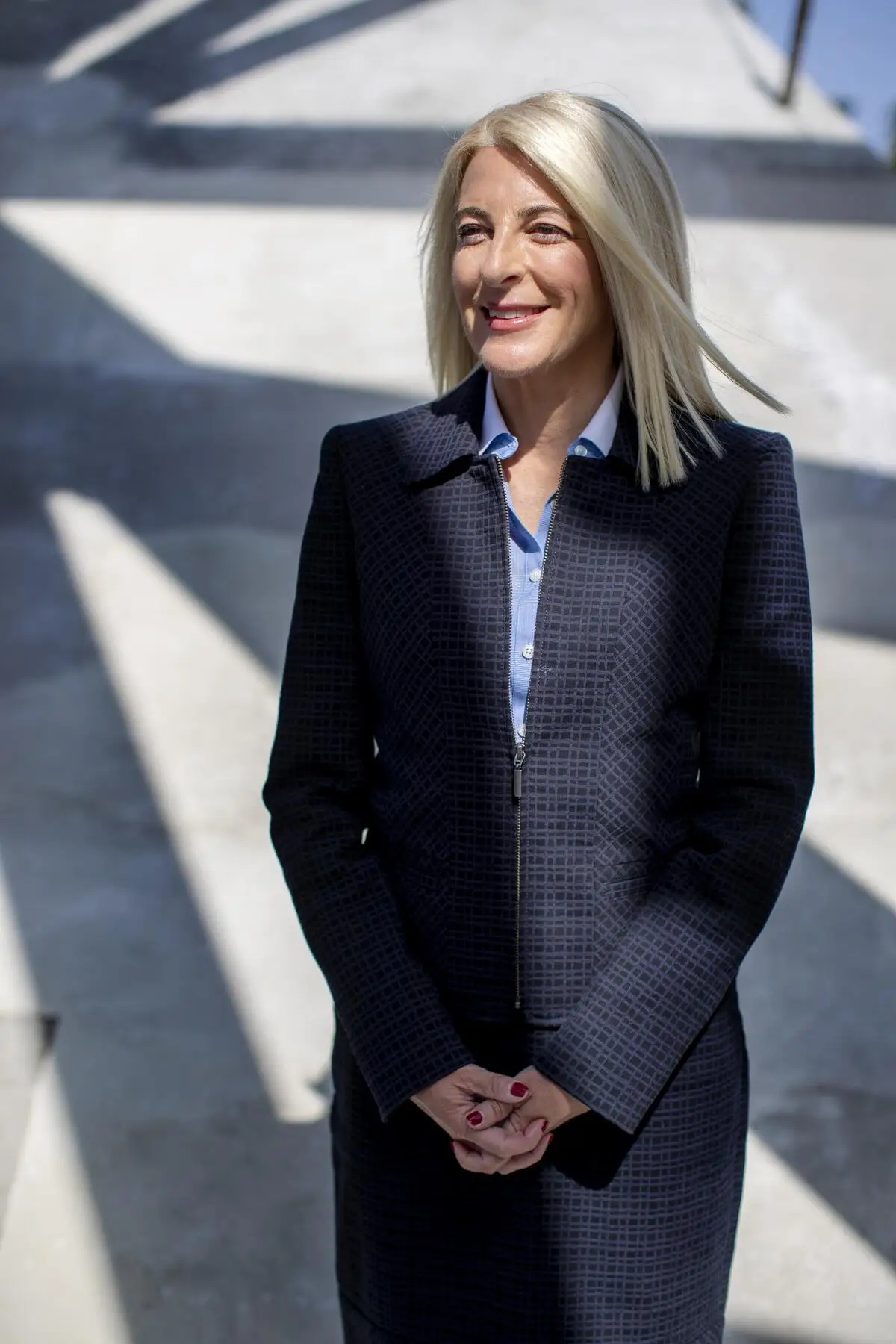 A smiling blond woman in a navy suit stands outside