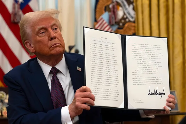 President Donald Trump holds up a signed executive order whilst sitting at his desk in the oval office