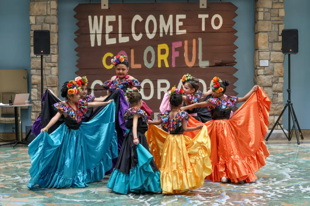 A group of young girls in traditional MExican folklorico dance attire dance in a circle together.