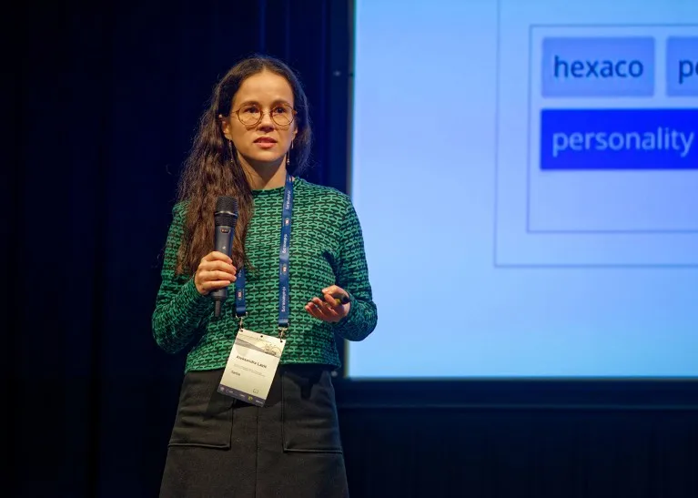 A woman holds a microphone while giving a talk