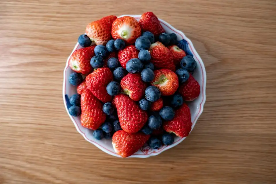 A bowl of fresh strawberries and blueberries on a wooden surface, showcasing a mix of textures