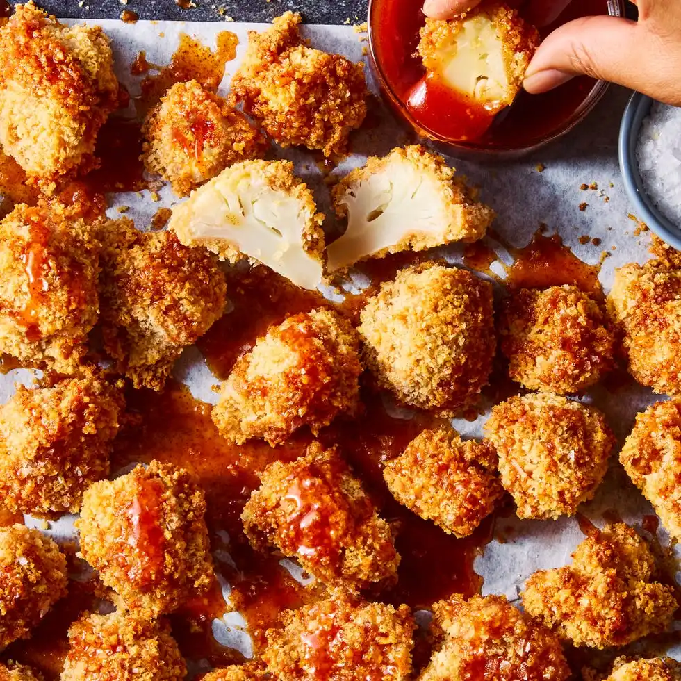 Crispy hot honey cauliflower nuggets crispy hot honey cauliflower nuggets on white parchment paper with one being dipped into sauce