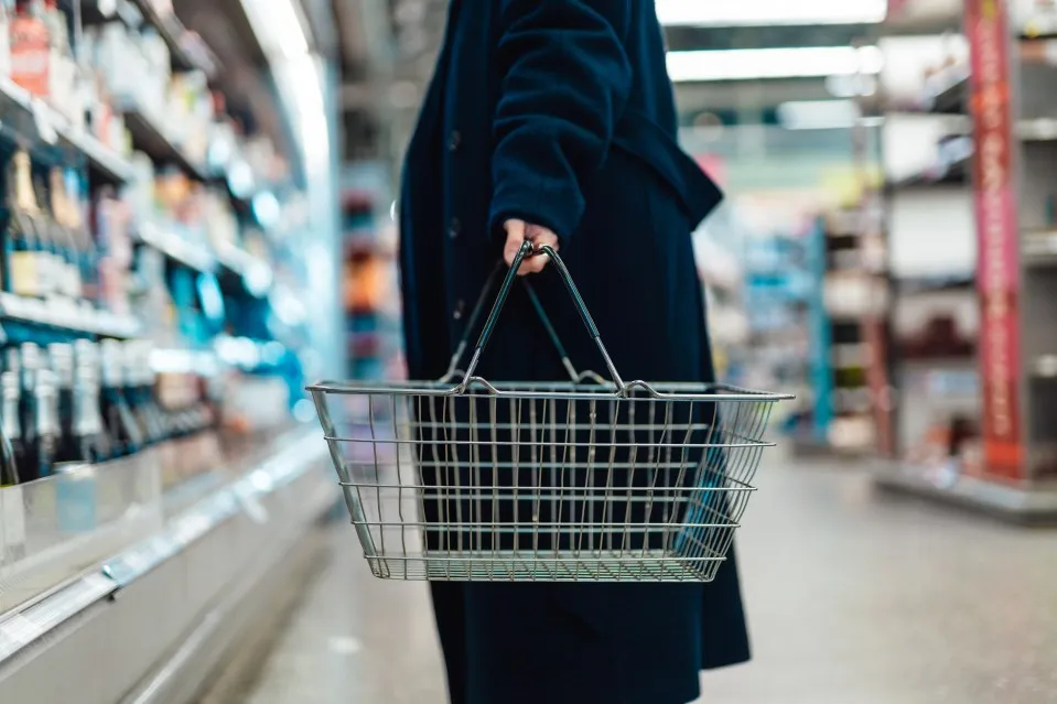 Woman carrying an empty shopping basket in a supermarket.