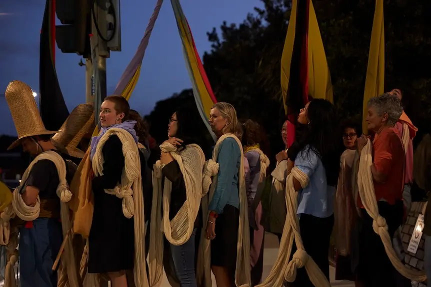 Women hold a large piece of gauze material between then on a darkening night.