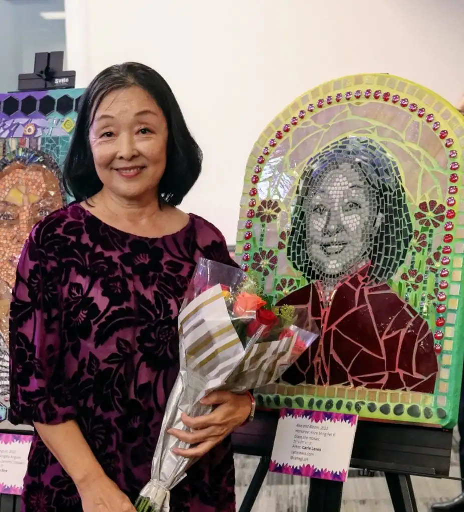 A Latina woman poses with an artwork depicting herself