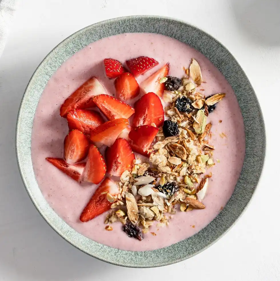 strawberry smoothie bowl with granola on white rustic table, healthy summer breakfast, high angle view
