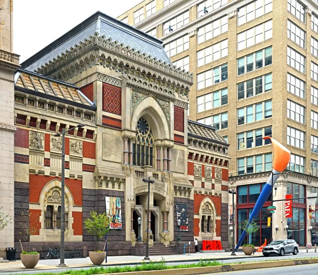 Historic building with ornate facade and giant paintbrush sculpture outside, flanked by modern office buildings.