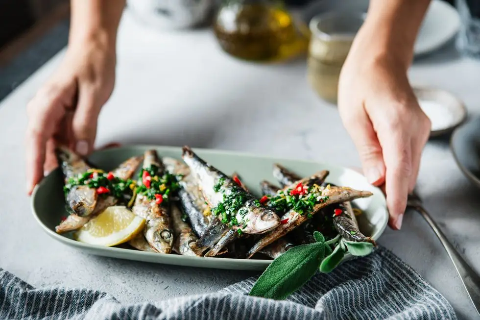 woman's hand serving fried fish with lemon on dining table