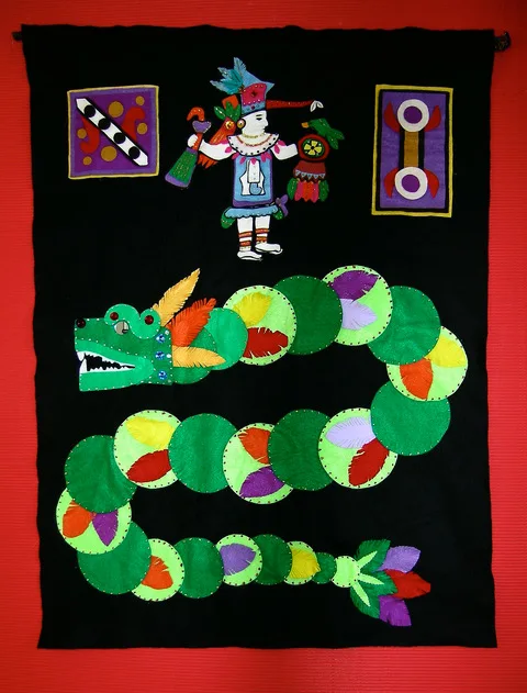 A fabric tapestry depicting a figure in traditional indegenous attire with a large Quetzalcoatl, or "Plumed Serpent" below him.