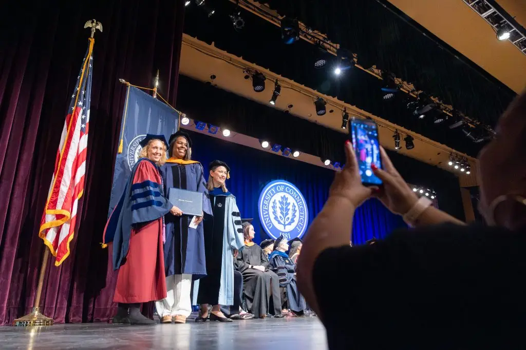 A person taking a photo of a graduate with their diploma