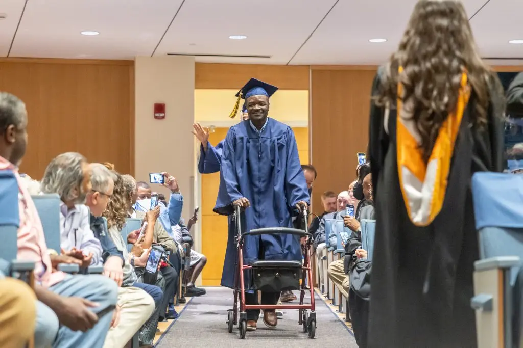An older graduate in his cap and gown walking down the isle with his walker