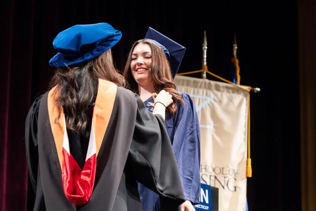 Graduates of the UConn School of Nursing have orange ribbons put on their regalia as the walk across the stage