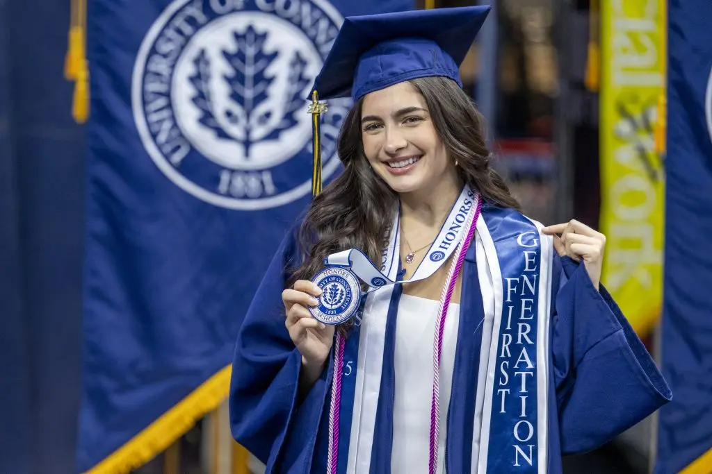 A student in her commencement cap and gown showing off her graduation medal