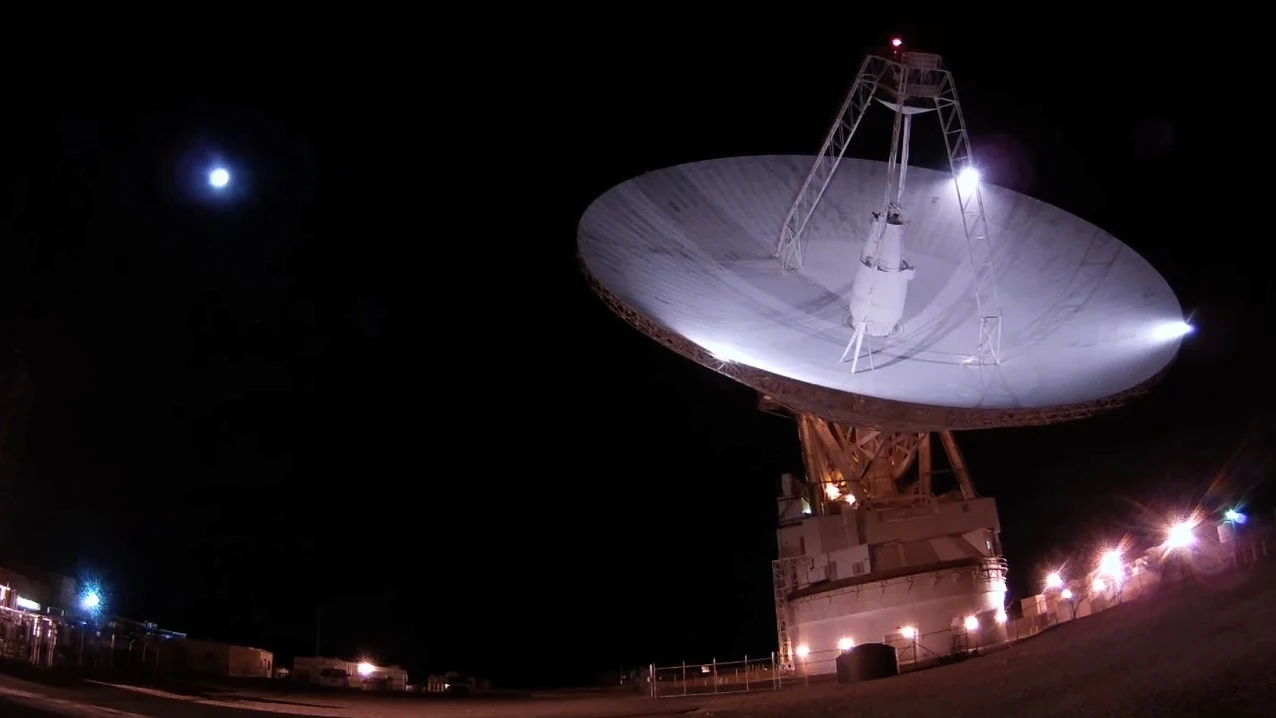 a large white radar dish points upward towards the sky at night