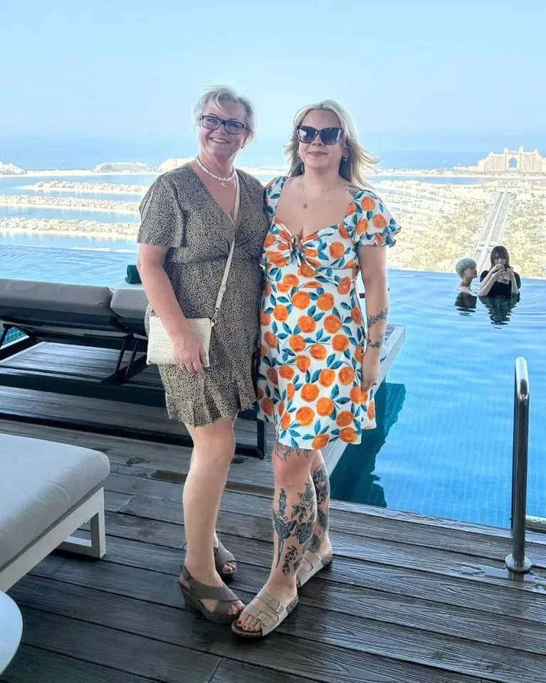 Two women in dresses stand by an infinity pool overlooking a city.