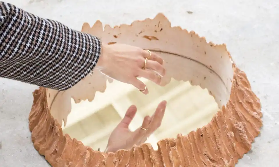 Hand hovering over a circular mirror with a 3D frame build around it to make it look like an orange crater.