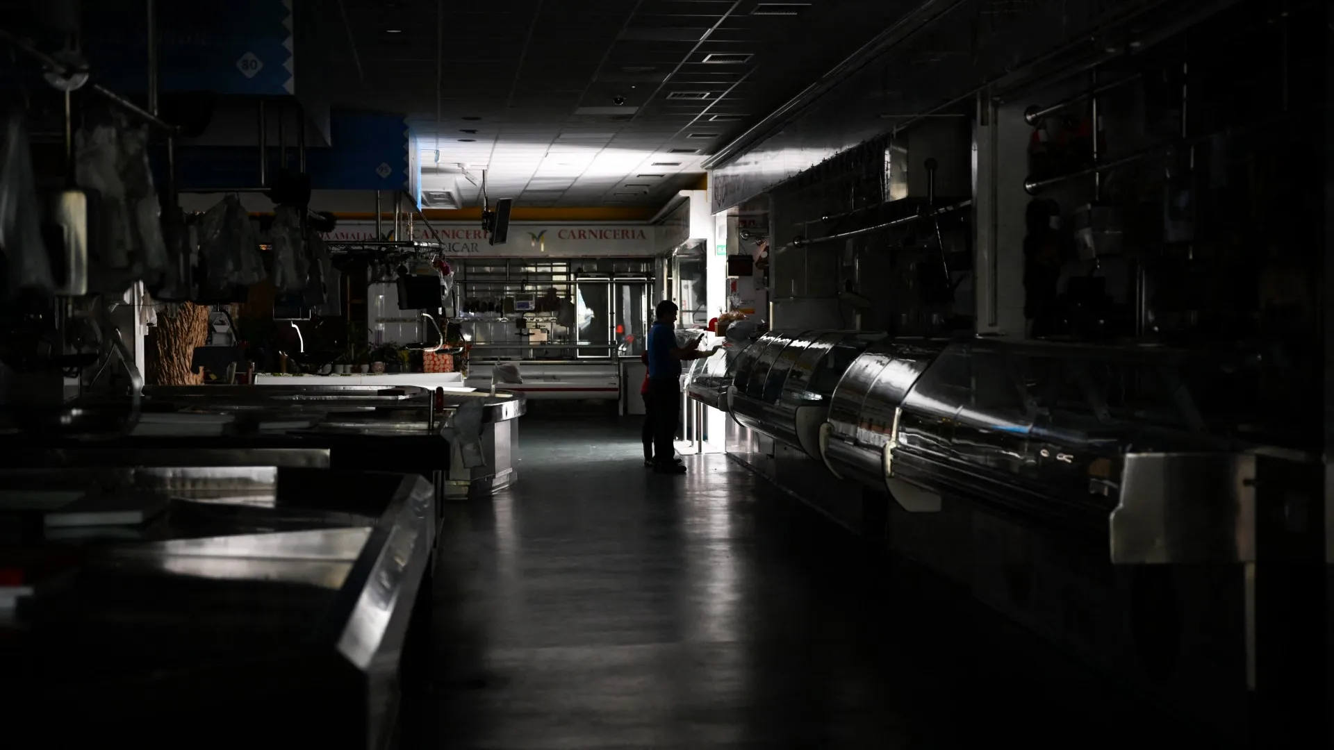 a lone person stands silhouetted by the light of an open door in a dark supermarket