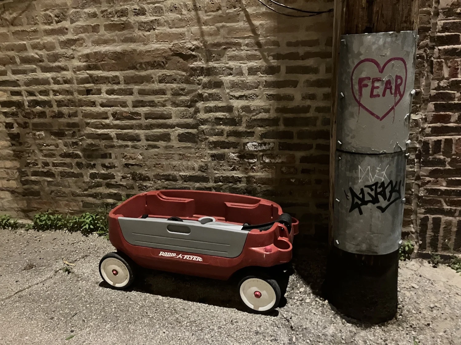 A red wagon next to a telephone pole in an alleyway.