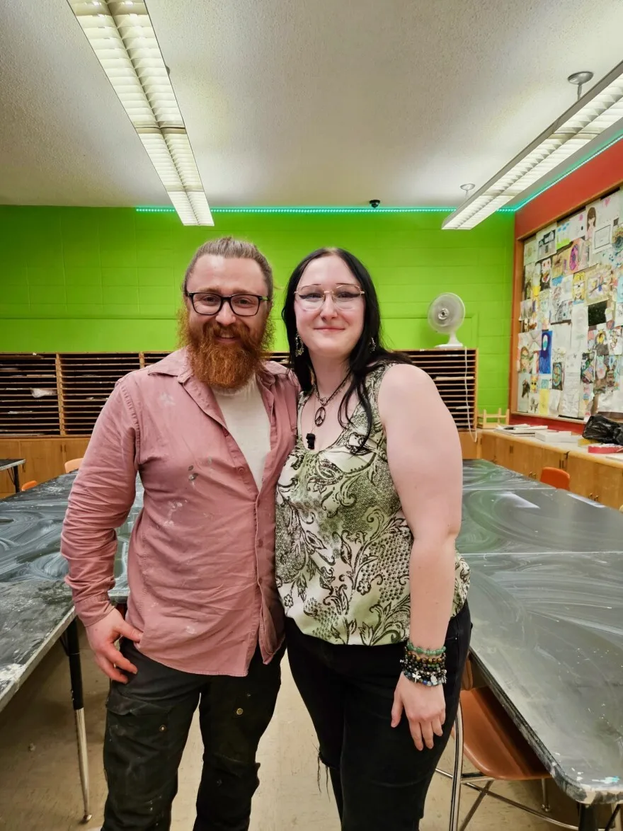 A man with an orange beard and glasses standing next to a woman with black hair and glasses