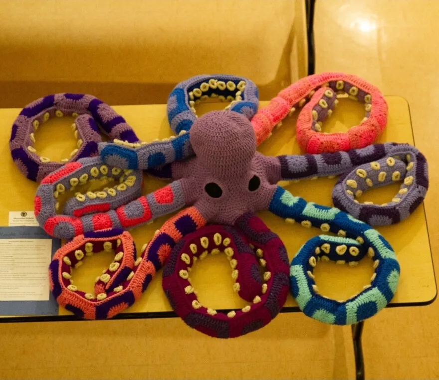 A crocheted octopus with green, blue, orange, purple, maroon, grey, and pink tentacles.