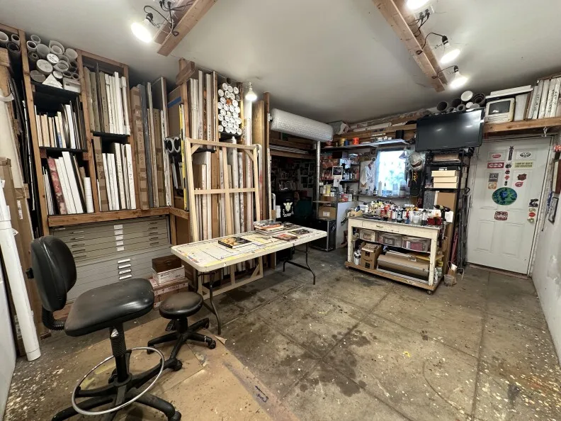 A room with two chairs and shelves full of paintings, stacked next to each other