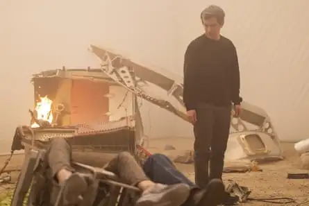 A man with greying gair looks down at some people who are collapsed on the floor, their faces out of shot, with wrecked material behind them