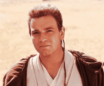 Character with short hair and braid in a brown robe looks forward thoughtfully, set against a desert-like background