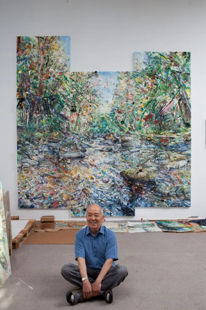 man seated cross-legged in front of large landscape composition