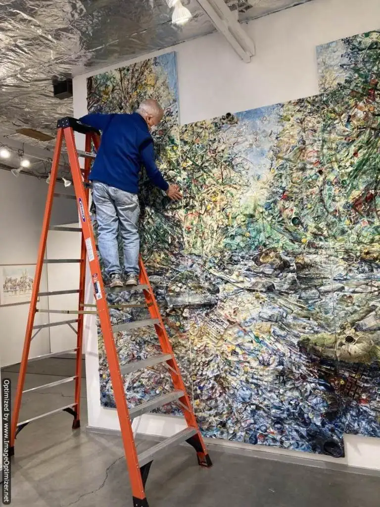 Man on ladder in front of large-scale painting with multi-paneled shape
