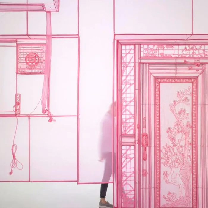 A detail of a sculpture showing part of a transparent pink ‘room’ with a shadowy figure inside. The door of the room is also transparent but decorative. 