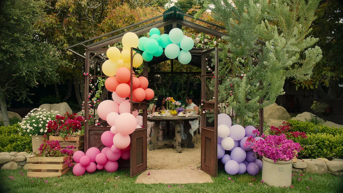 Mindy Kaling and Meghan having tea under a balloon arch.