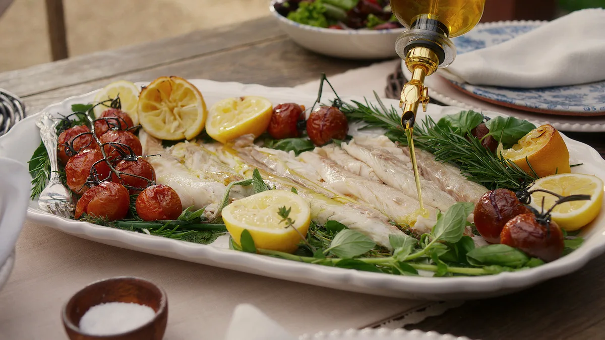 Salt-baked fish with roasted tomatoes getting drizzled with olive oil.