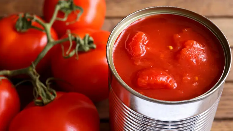 An open can of tomatoes next to fresh tomatoes