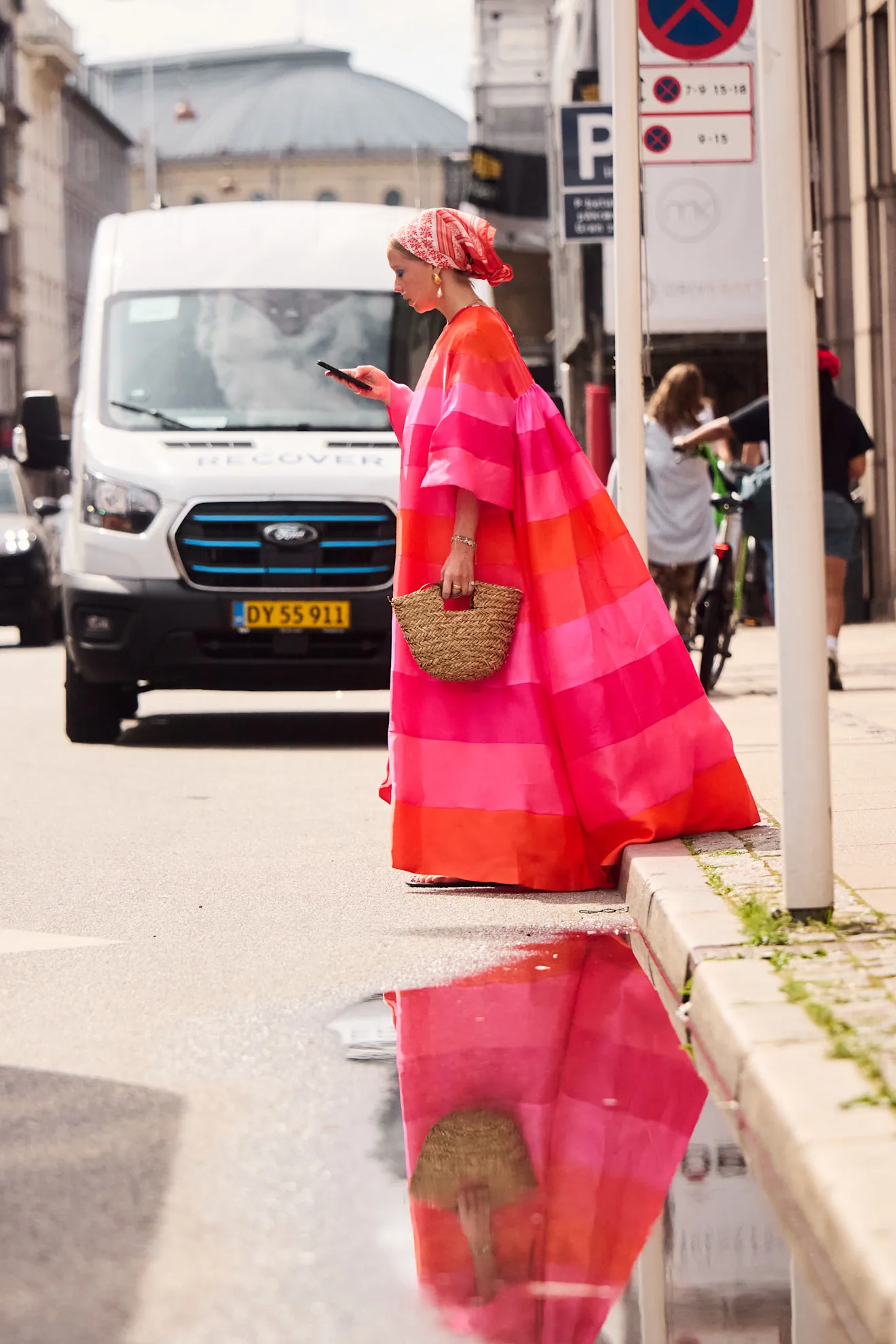 a woman wearing a pink and orange striped dress in a bandana and straw bag