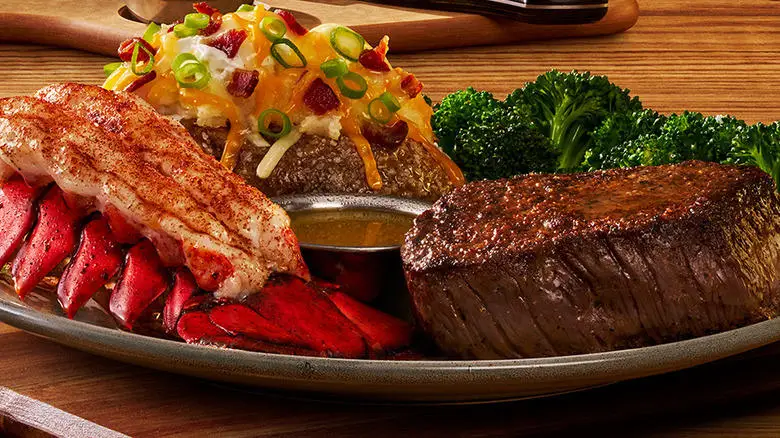 Closeup of an Outback Steakhouse meal with steak, lobster tail, a loaded baked potato, and broccoli